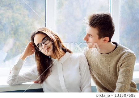 Unhappy female learner sitting near window in campus looking sick and tired. Her boyfriend trying to hug her and calm her down, but she refused his help 131507688