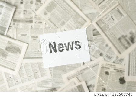 Lots of old newspapers lay on surface with a white paper with inscription NEWS in the middle. Blurred 131507740