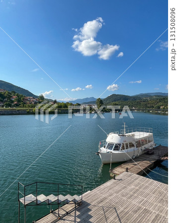 A white boat moored on a wooden pier on the Drina River, surrounded by hills and a village A white boat moored on a wooden pier on the Drina River, surrounded by hills and a village 131508096