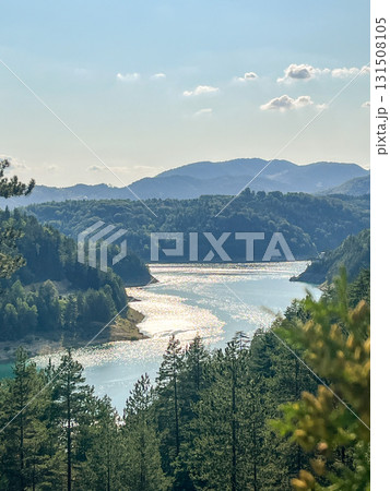 Panoramic top view of mountain river reflecting sunlight surrounded by dense green forest  131508105