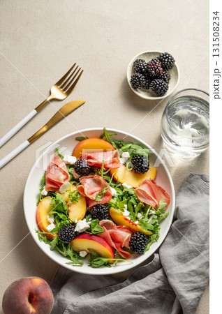 Fresh salad with peaches, arugula, feta, prosciutto and berries in a plate on a light background 131508234