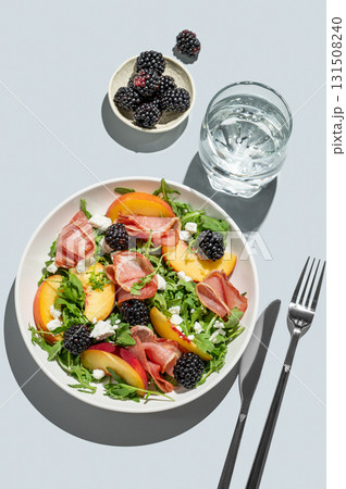 Salad with peaches, arugula, feta, prosciutto and berries in a plate on a blue background Salad with peaches, arugula, feta, prosciutto and berries in a plate on a blue background 131508240