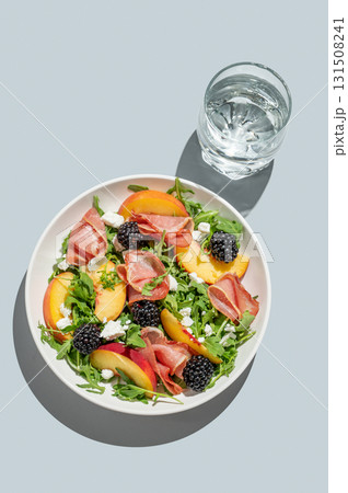 Salad with peaches, arugula, feta, prosciutto and berries in a plate on a blue background Salad with peaches, arugula, feta, prosciutto and berries in a plate on a blue background 131508241