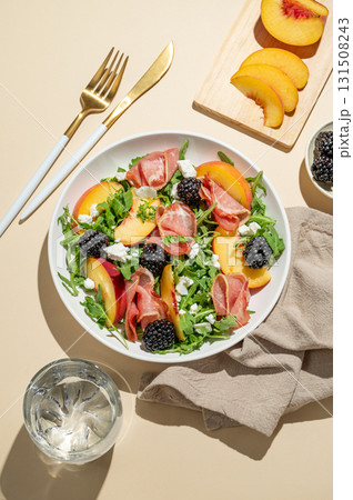 Salad with peaches, arugula, feta, prosciutto and berries in a plate on a yellow background Salad with peaches, arugula, feta, prosciutto and berries in a plate on a yellow background 131508243
