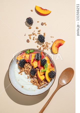 Natural greek yogurt with granola or muesli, peach and blackberry in a bowl on a beige background 131508251
