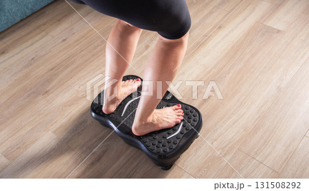 Women's legs stand on a sports vibration platform at home. Concept of doing sports at home. Modern home exercise machine, close-up Women's legs stand on a sports vibration platform at home. Concept of doing sports at home. Modern home exercise machine, close-up 131508292