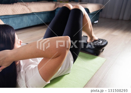 A young girl is doing sports on a vibration platform exercise machine at home in a home environment. The concept of getting rid of excess weight and cellulite. Sports device A young girl is doing sports on a vibration platform exercise machine at home in a home environment. The concept of getting rid of excess weight and cellulite. Sports device 131508293