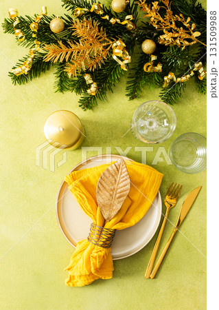 Top view of a Christmas table, featuring an empty plate, folded napkin, and cutlery. Spruse branches and golden Christmas tree ornaments add a touch of elegance and seasonal charm Top view of a Christmas table, featuring an empty plate, folded napkin, and cutlery. Spruse branches and golden Christmas tree ornaments add a touch of elegance and seasonal charm 131509988