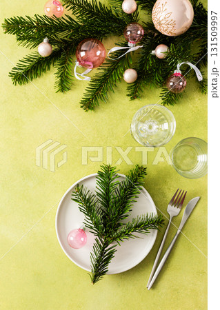 Top view of an elegant Christmas table with an empty plate and cutlery on a vibrant green background. Spruse branches and pink tree decorations add seasonal charm Top view of an elegant Christmas table with an empty plate and cutlery on a vibrant green background. Spruse branches and pink tree decorations add seasonal charm 131509997