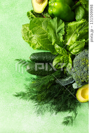 A variety of fresh green vegetables and herbs are arranged neatly on a bright green surface. Among them are cucumbers, broccoli, leafy greens, avocado, and basil, perfect for healthy cooking or salads A variety of fresh green vegetables and herbs are arranged neatly on a bright green surface. Among them are cucumbers, broccoli, leafy greens, avocado, and basil, perfect for healthy cooking or salads 131509998