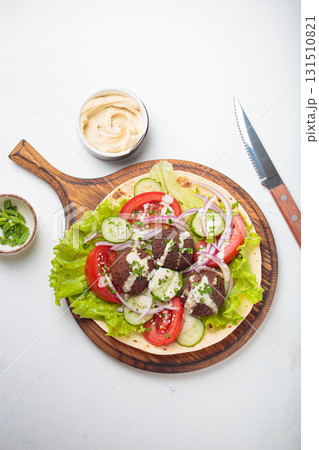 Preparing and cooking falafel wrap on pita on wooden cutting board with hummus top view white background 131510821