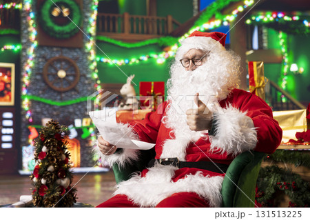Santa Claus gives cheerful thumbs up while reading festive Christmas letters, answering requests. Man wearing xmas red suit looks at wish lists to fulfill kids hopes, doing positive hand gesture Santa Claus gives cheerful thumbs up while reading festive Christmas letters, answering requests. Man wearing xmas red suit looks at wish lists to fulfill kids hopes, doing positive hand gesture 131513225