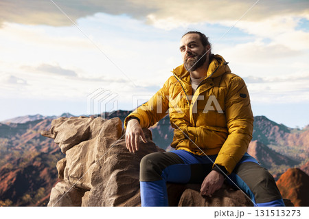 Traveler stands alone at the edge of a towering mountain range, gazing at the clouds and stunning panoramic scenery. Pleased hiker showcasing personal growth and perseverance. 131513273