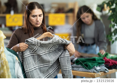 Female shopper chooses beautiful checkered coat-jacket in clothing store Female shopper chooses beautiful checkered coat-jacket in clothing store 131515016