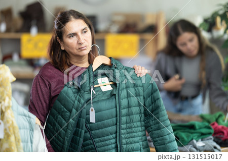 Female shopper chooses winter down coat in clothing store 131515017