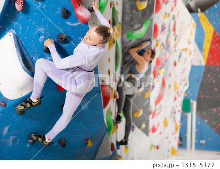Focused sporty young woman climbing on bouldering wall 131515177