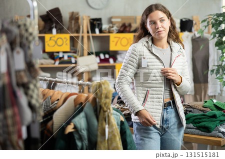 During November sales, young woman choose and try on down coat, view reflection in mirror. During November sales, young woman choose and try on down coat, view reflection in mirror. 131515181