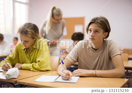 Boys and girls sitting at desk in classroom full of pupils during lesson Boys and girls sitting at desk in classroom full of pupils during lesson 131515230