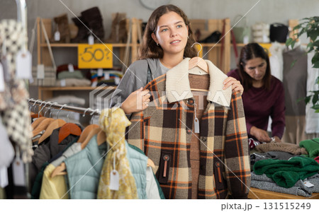 Girl tries on fashionable checkered coat-jacket in clothing boutique 131515249