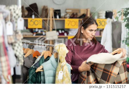 Female shopper chooses beautiful checkered coat-jacket in clothing store Female shopper chooses beautiful checkered coat-jacket in clothing store 131515257