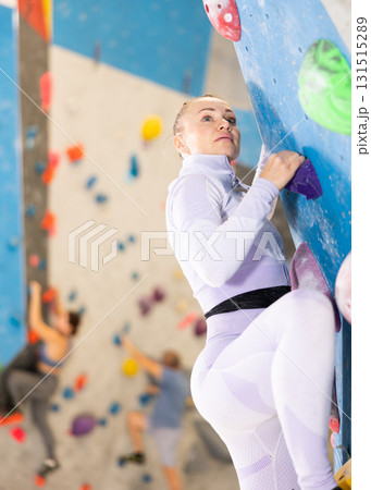 Young female alpinist practicing indoor rock-climbing on artificial boulder without safety belts Young female alpinist practicing indoor rock-climbing on artificial boulder without safety belts 131515289