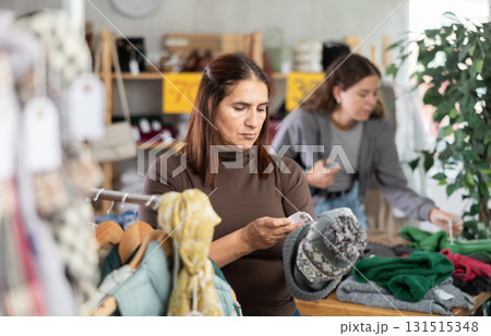During November sales, Latin woman choose hat, other client in background During November sales, Latin woman choose hat, other client in background 131515348