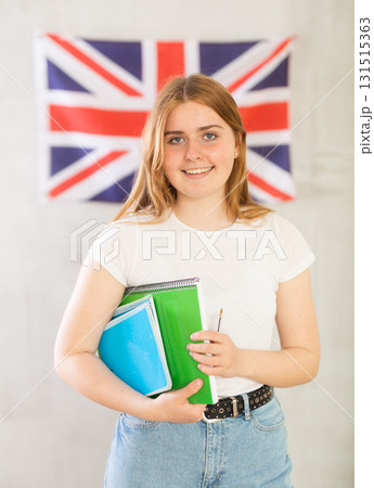 Female student with notebooks stands against wall under flag of Great Britain. Gray background Female student with notebooks stands against wall under flag of Great Britain. Gray background 131515363