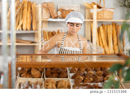 Young female seller putting croissant in bag 131515366