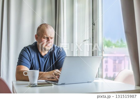 Man working on laptop at home with coffee by the window. Man working on laptop at home with coffee by the window. 131515987