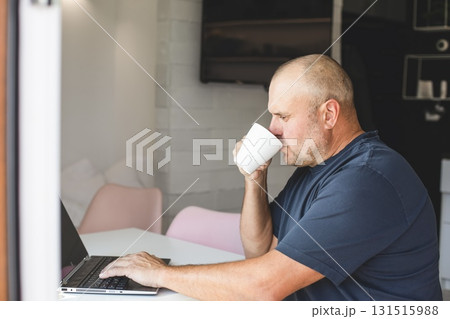 Man working on laptop at home with coffee by the window. Man working on laptop at home with coffee by the window. 131515988