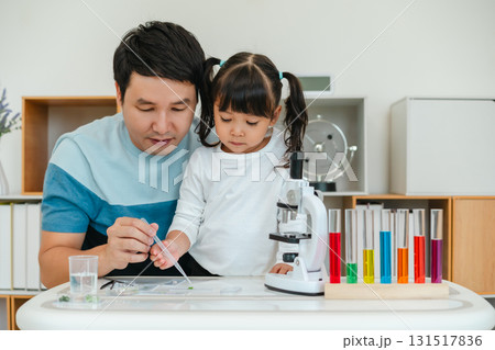 toddler girl scientist using pipette dropping of liquid being placed on glass slide with her father, preparing specimen for science microscope 131517836