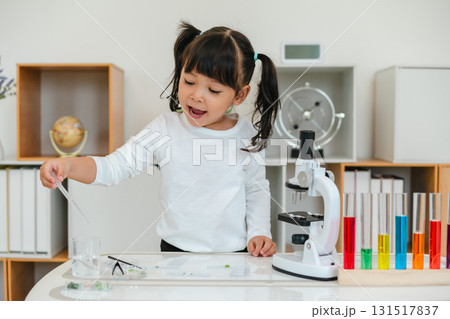 toddler girl scientist is using a pipette to draw liquid from a beaker in order to prepare slide for the microscope. preparing specimen for science 131517837