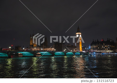 Illuminated Big Ben and Houses of Parliament at night with Westminster Bridge spanning the River Thames, green lights reflecting on the water. 131518723