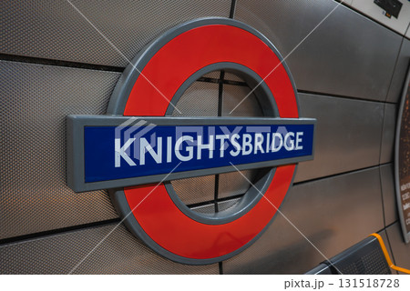 The iconic Knightsbridge station roundel sign is displayed on a metallic, textured wall. The red frame and blue bar showcase classic London Tube design. 131518728