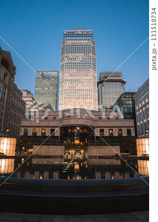 Twilight view of Canary Wharf in London, featuring One Canada Square and modern skyscrapers, with a reflective water feature and plaza in the foreground. 131518734