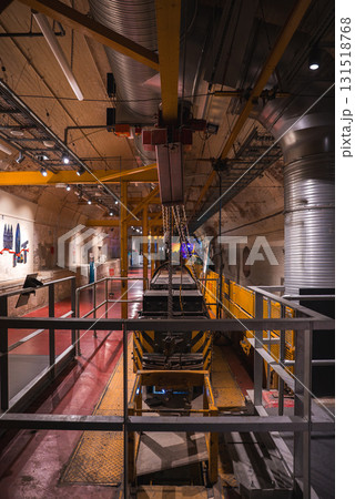 Tunnel like industrial interior featuring yellow metal beams, chains, a conveyor system, curved walls with pipes, and informational displays in London. Tunnel like industrial interior featuring yellow metal beams, chains, a conveyor system, curved walls with pipes, and informational displays in London. 131518768