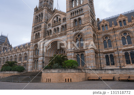 The grand facade of the Natural History Museum in London features Romanesque architecture, arched windows, and towers, with greenery and benches in the foreground. The grand facade of the Natural History Museum in London features Romanesque architecture, arched windows, and towers, with greenery and benches in the foreground. 131518772