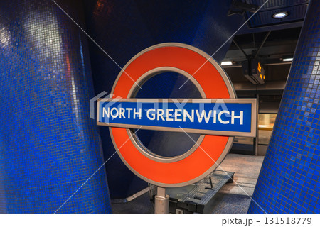 The London Underground roundel for North Greenwich station is displayed against deep blue tiled walls, with modern lighting and a digital display board visible. 131518779