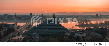 Morning view of Riga, Latvia, featuring the National Library, historic church spires, the Daugava River, and the arched railway bridge in soft mist. 131518794