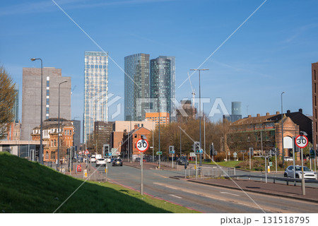 Daytime view of Manchester featuring Deansgate Square towers, historic brick buildings, a busy street with traffic signs, and a grassy embankment. 131518795