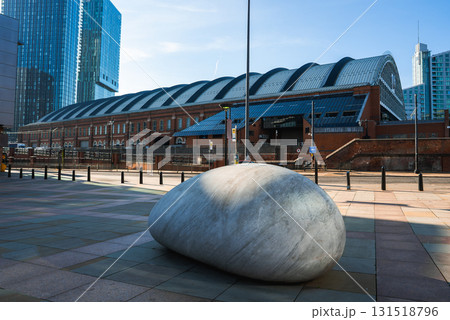 The Manchester Central Convention Complex with its arched roof and red brick facade, a stone sculpture in the plaza, and modern skyscrapers in the background. 131518796