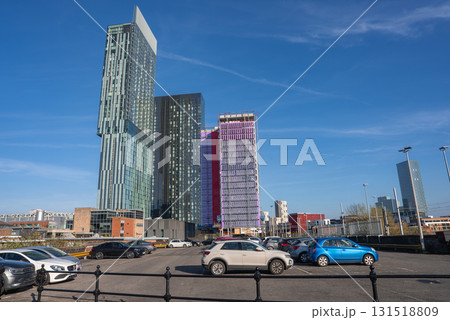 View of Manchester featuring a parking lot with parked cars in the foreground and modern skyscrapers, including Beetham Tower, under a clear blue sky. View of Manchester featuring a parking lot with parked cars in the foreground and modern skyscrapers, including Beetham Tower, under a clear blue sky. 131518809