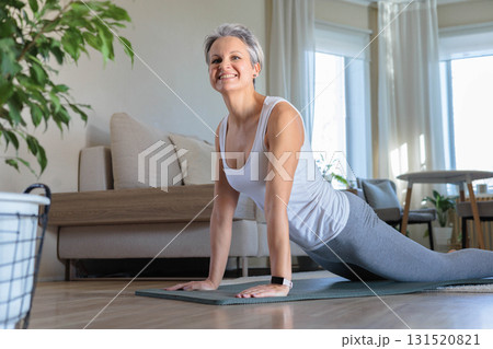 Beautiful smiling gray-haired mature middle-aged woman at home on a yoga mat doing stretching, yoga. Beautiful smiling gray-haired mature middle-aged woman at home on a yoga mat doing stretching, yoga. 131520821