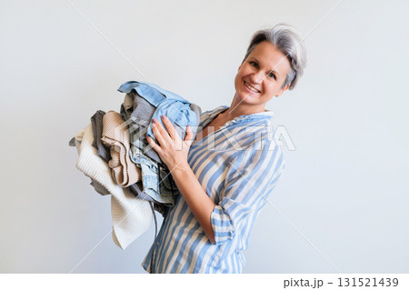 Mature gray haired woman holding stack of clothes isolated on white background Mature gray haired woman holding stack of clothes isolated on white background 131521439