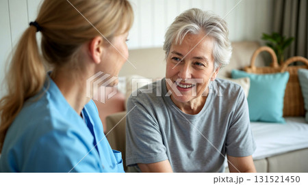 A cheerful female caregiver providing emotional support to a happy elderly woman at home. 131521450