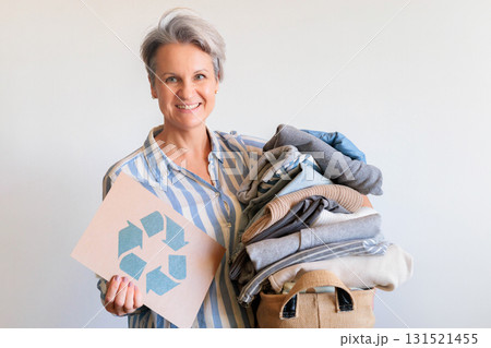 Gray haired woman with pile of clothes and recycling reusing signboard isolated on white background Gray haired woman with pile of clothes and recycling reusing signboard isolated on white background 131521455
