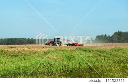 A modern tractor with a new cultivator cultivates the soil in a field before planting crops against a blue summer sky. Agricultural work on a collective farm. Copy space for text A modern tractor with a new cultivator cultivates the soil in a field before planting crops against a blue summer sky. Agricultural work on a collective farm. Copy space for text 131522823
