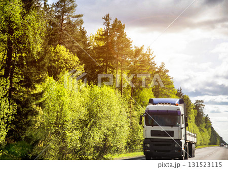 Modern truck transports cargo against the backdrop of forest and sun in summer, beautiful sky with clouds. Logistics company delivering cargo on international routes. Copy space for text. Freight Modern truck transports cargo against the backdrop of forest and sun in summer, beautiful sky with clouds. Logistics company delivering cargo on international routes. Copy space for text. Freight 131523115