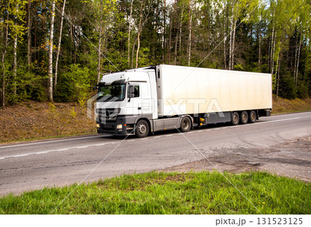 A truck with a refrigerated semi-trailer transports refrigerated cargo along a country road against the backdrop of beautiful nature and forest in summer. Copy space for text A truck with a refrigerated semi-trailer transports refrigerated cargo along a country road against the backdrop of beautiful nature and forest in summer. Copy space for text 131523125