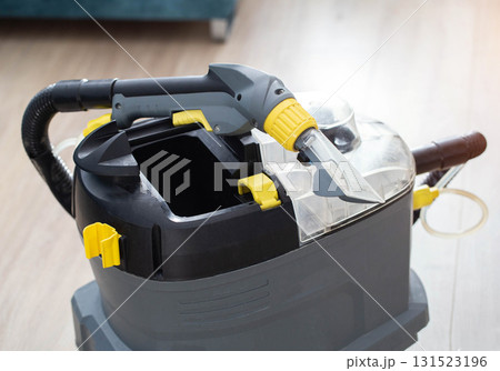 A modern upholstery vacuum cleaner stands in a room against a sunset backdrop. Cleaning service. Copy space for text, housework A modern upholstery vacuum cleaner stands in a room against a sunset backdrop. Cleaning service. Copy space for text, housework 131523196